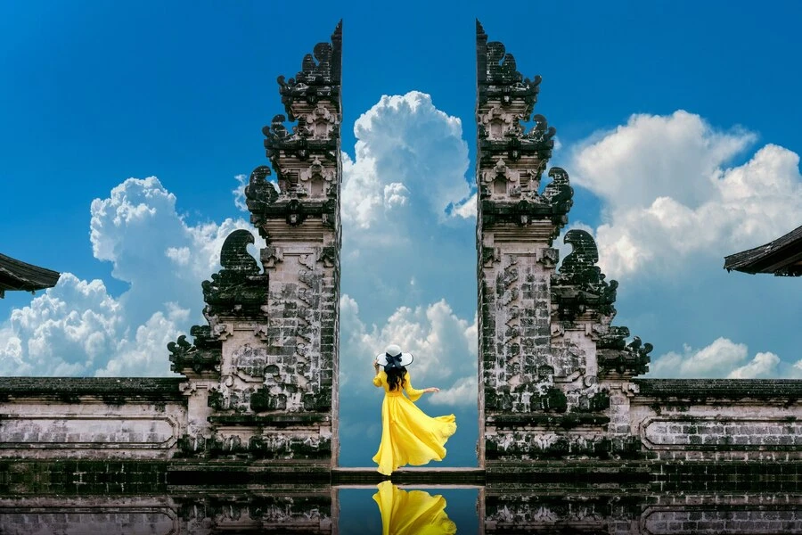 Woman in yellow dress at a split gate under blue sky with clouds.