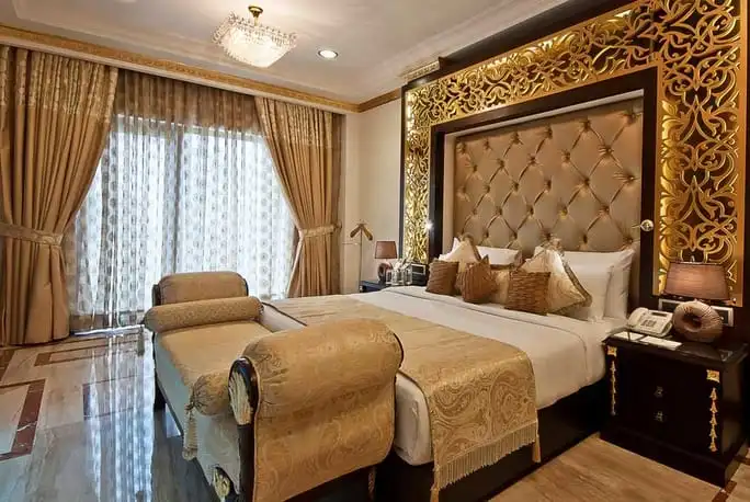 Opulent bedroom with gold accents, large bed, ornate headboard, and elegant curtains.