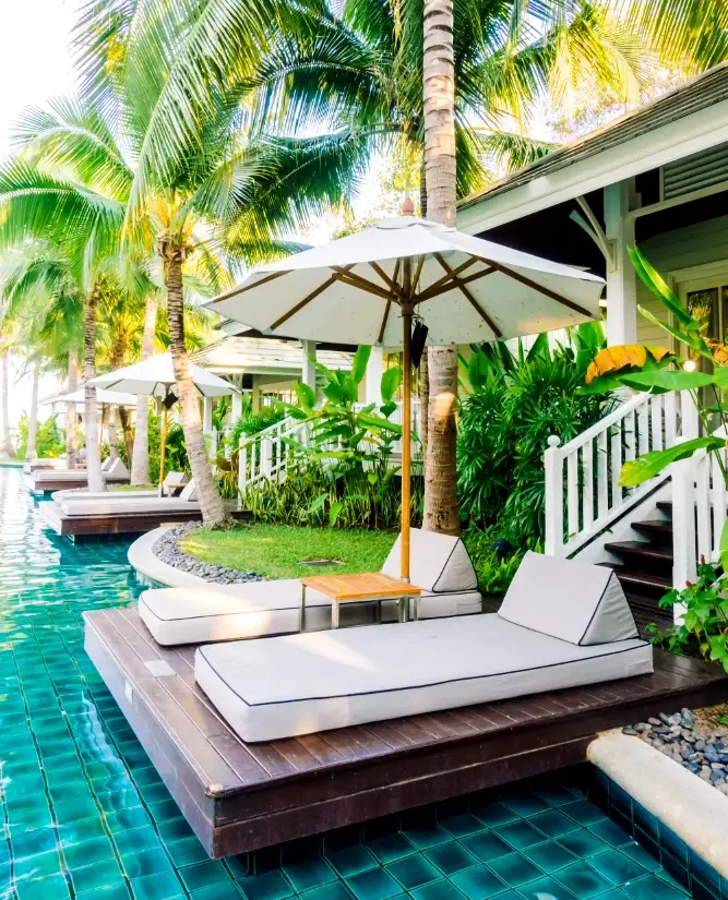 Poolside loungers and umbrella by a tropical resort villa, surrounded by lush greenery.
