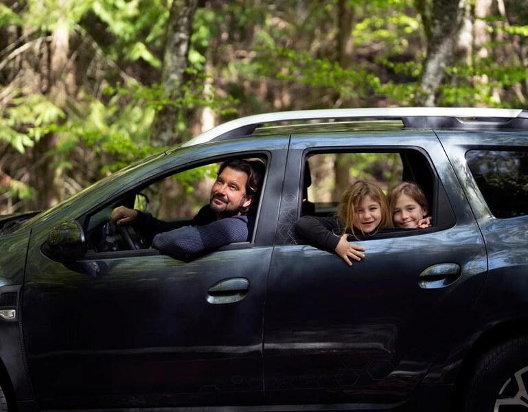 Black SUV with two passengers, parked in a wooded area, perfect for family road trips.