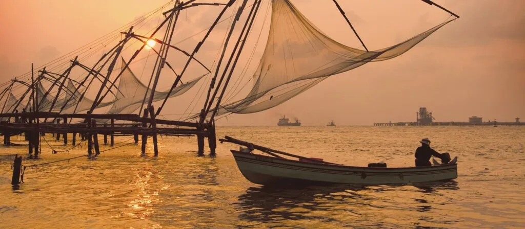 Sunset at a harbor with silhouette of traditional fishing nets and a man in a boat.
